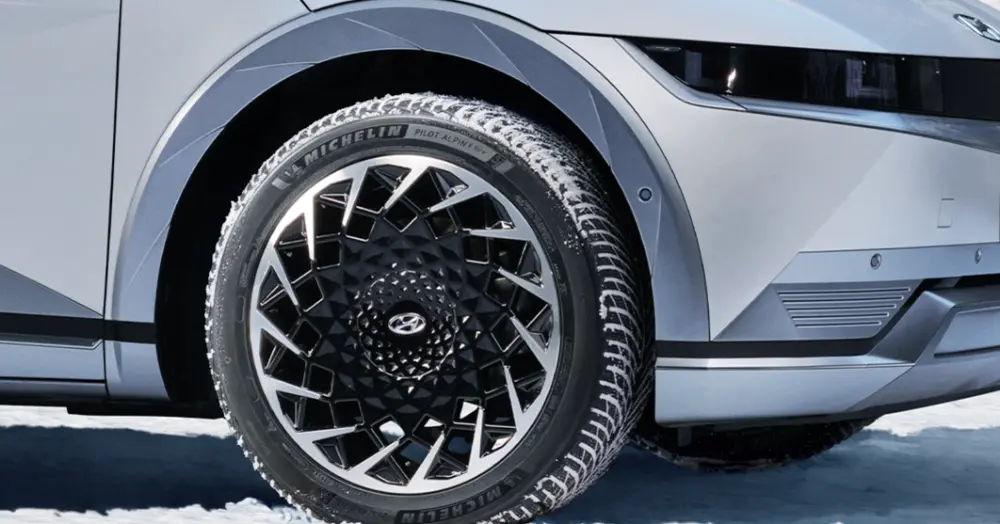 Prim-plan al unei anvelope de iarnă montate pe un vehicul electric Hyundai argintiu, cu jantă din aliaj cu design geometric, pe un drum înzăpezit.