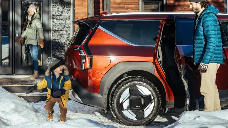 Eine Familie lädt im Schnee ihr Gepäck aus einem Kia-SUV aus, der mit Michelin X-Ice North+ Reifen ausgestattet ist.