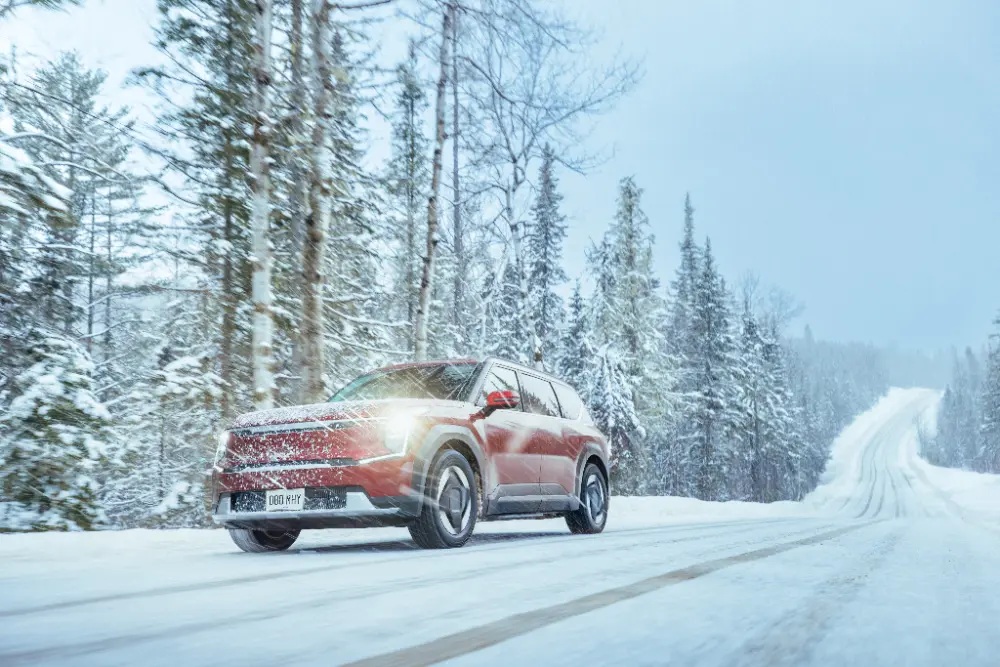 Röd SUV kör på snötäckt landsväg genom skog under snöfall.