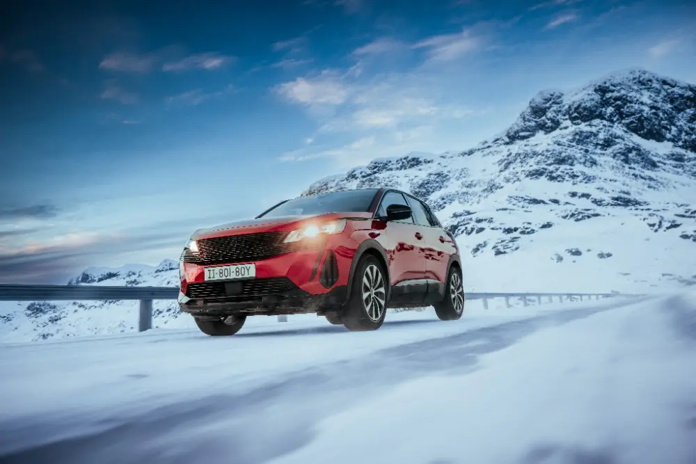 SUV rojo circulando por una carretera de montaña nevada, equipado con neumáticos de invierno para una conducción segura en frío.