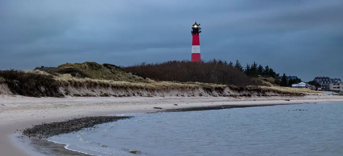 Ein rot-weiß gestreifter Leuchtturm erhebt sich über Dünen an einem norddeutschen Sandstrand in Hörnum