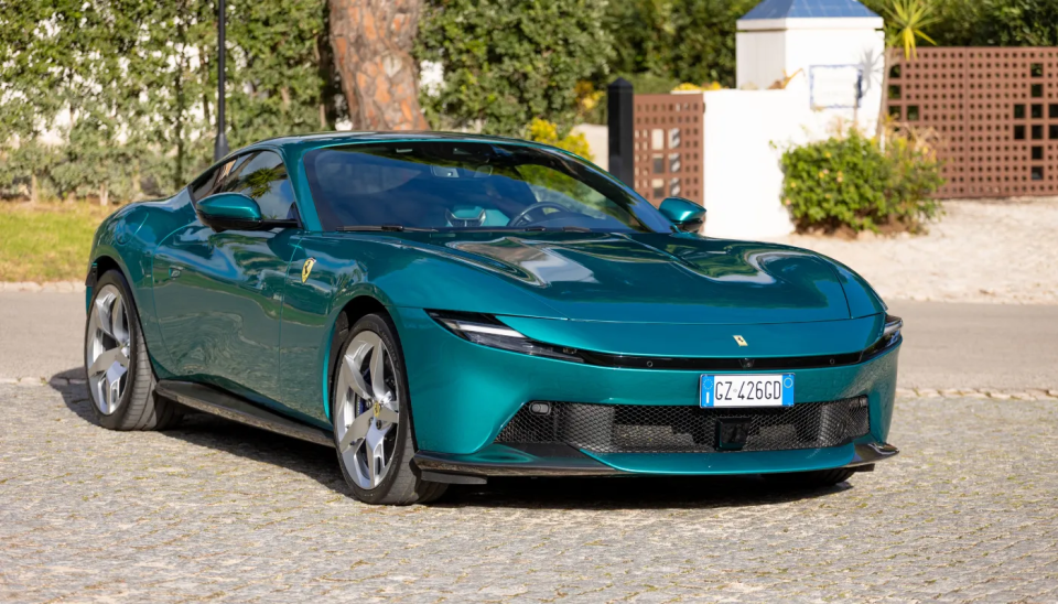 Ferrari Amalfi i metallic turkosgrön, framifrån, parkerad framför en medelhavsbyggnad med palmer.