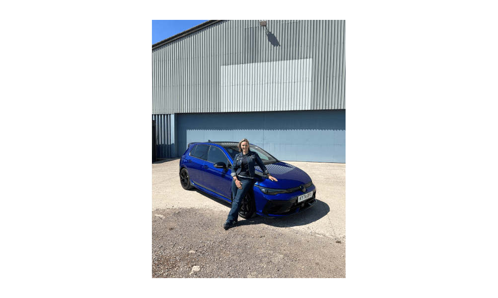 Vicki Butler-Henderson sitzt am Volkswagen Golf R MK8.5 vor einem Flugzeughangar