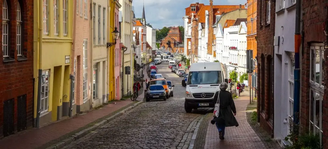 Eine gepflasterte Straße führt durch die Altstadt in Lübeck mit bunten Backsteinhäusern in Gelb, Rosa und Weiß