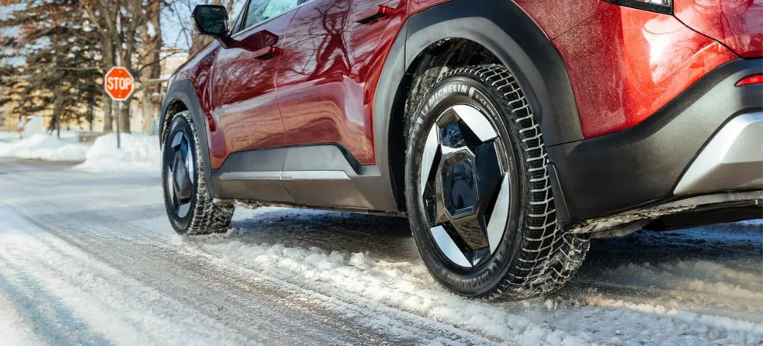 Un Kia roșu, echipat cu anvelope Michelin X-Ice Snow+, este parcat în fața unui semn de stop pe un drum acoperit de zăpadă