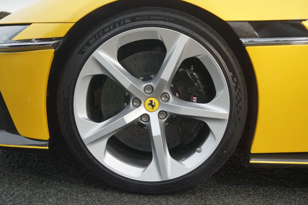 Cerchio in alluminio argentato montato su una Ferrari gialla, con dettaglio della pinza del freno e del logo