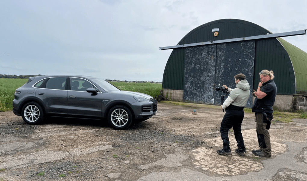 Dreh eines Porsche Cayenne Tests vor Ort, mit dem SUV geparkt vor einer rustikalen Scheune, während das Kamerateam cineastische Aufnahmen macht.