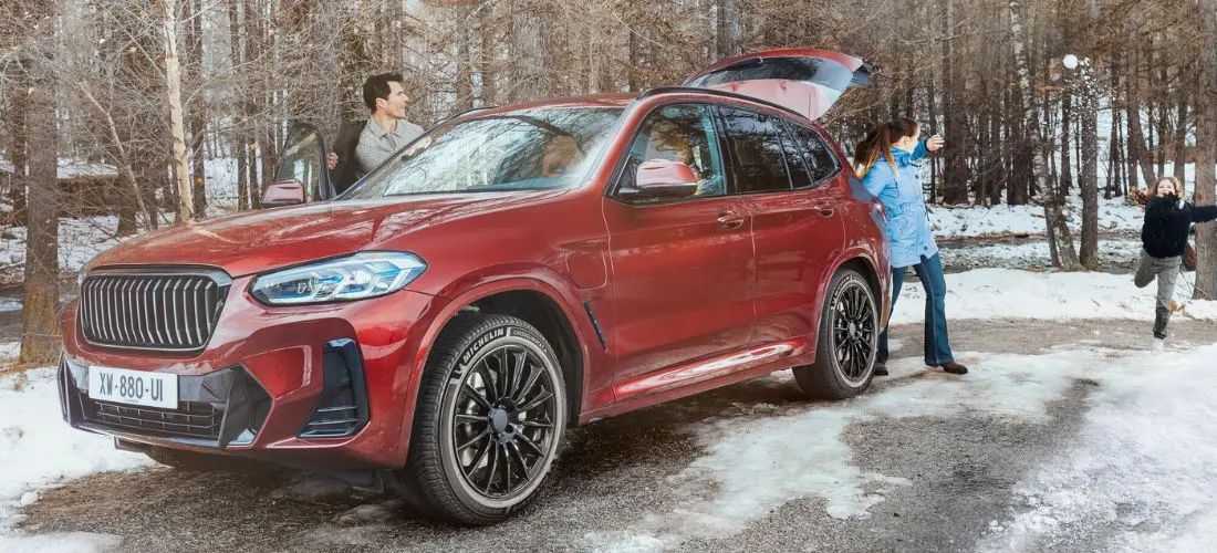 Ein roter SUV mit Michelin CrossClimate 3 parkt mit geöffneter Heckklappe an einem verschneiten Waldweg