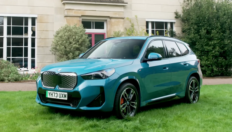 Ein Bild des BMW iX1, der auf Gras vor einem herrschaftlichen Anwesen geparkt ist